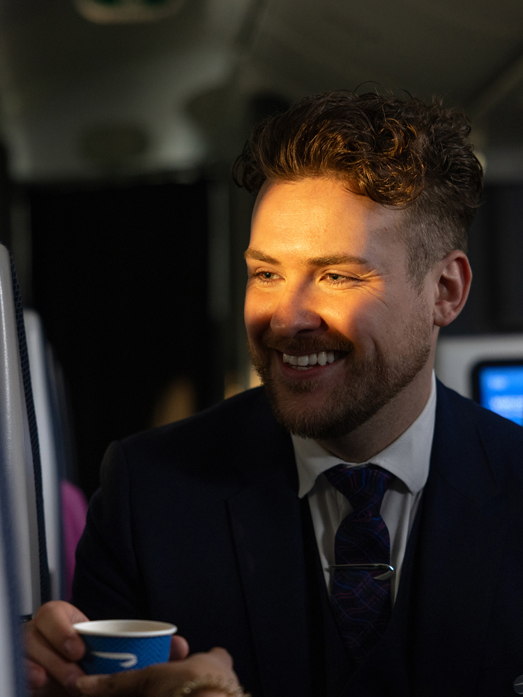 A friendly British Airways colleague offering a customer a drink.
