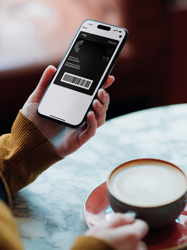 A woman looking at a British Airways Club card on her phone in a coffee shop.
