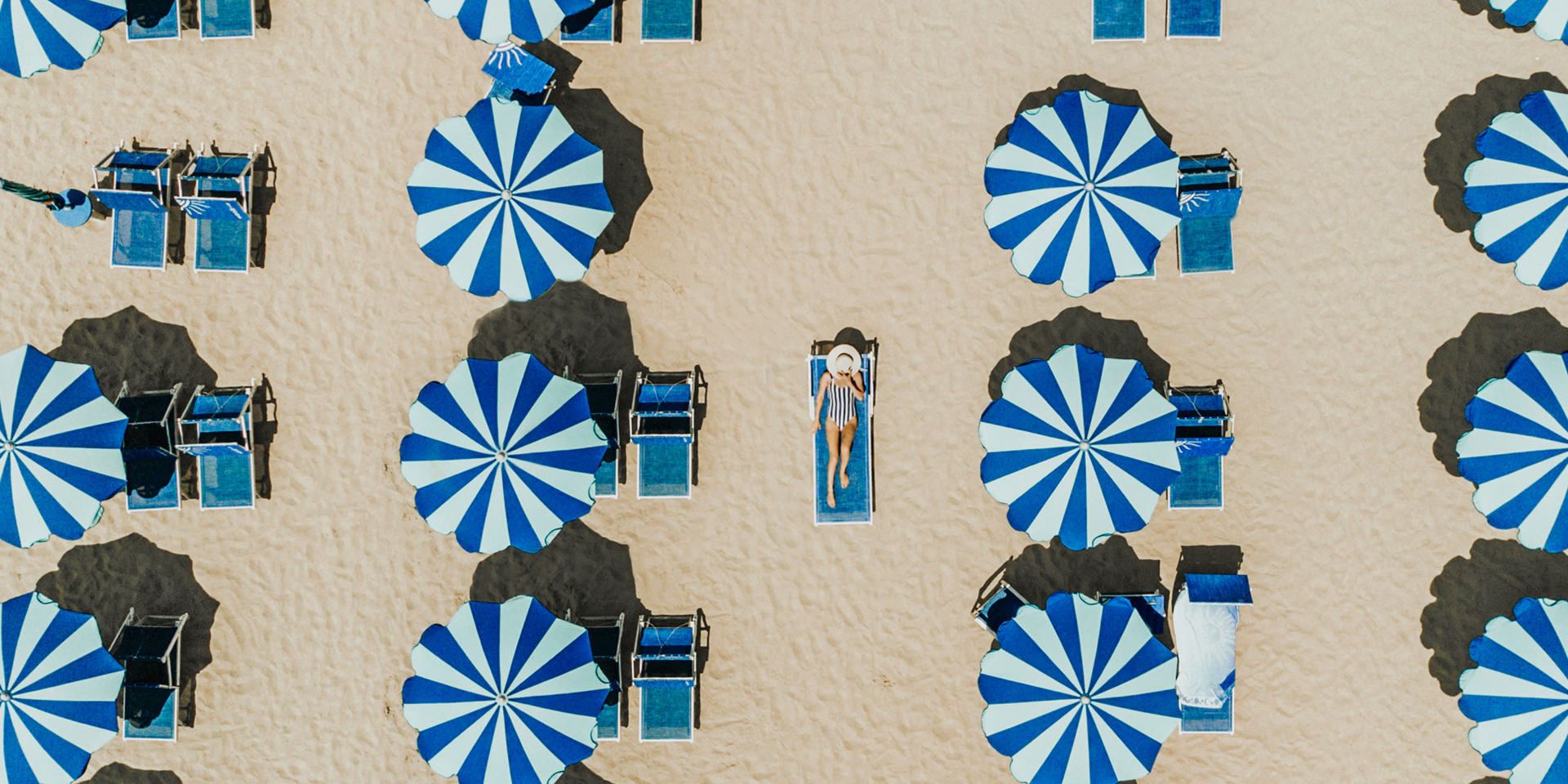 Blue and white parasols on a beach photographed from above.