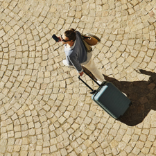 Overhead shot of a lady walking with a small wheeled suitcase.