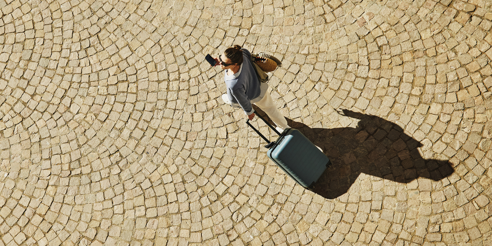 Overhead shot of a lady walking with a small wheeled suitcase.
