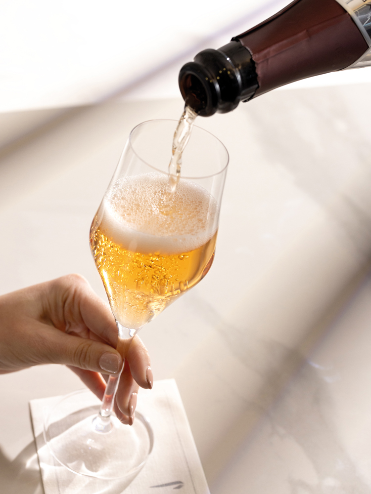 A class of sparkling wine being poured against a white background.