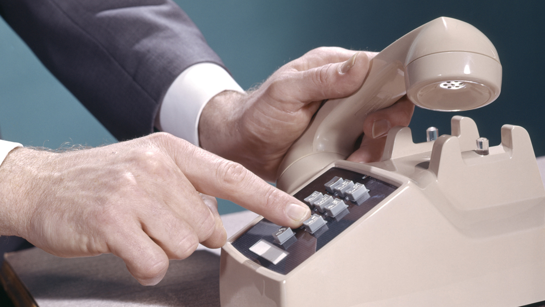 A close up of a man using a retro phone with a blue background.