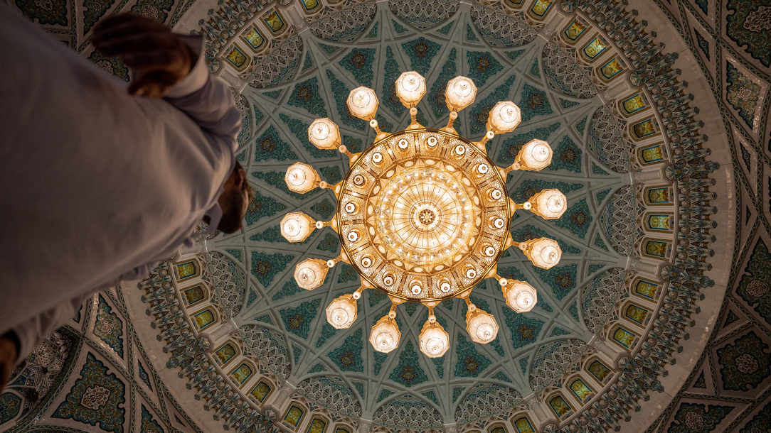A man looking up at the ceiling of the Grand Sultan Qaboos Mosque.